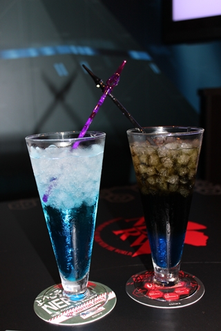 写真左から「Drink No.08　シンジのお酒『逃げちゃダメだ』（アルコール入り）／790円」ブルーリキュール×ソーダを合わせ、シンジのプラグスーツの色である青をベースにしたカクテル。これを飲めば初号機のパイロットになる勇気が出るとか出ないとか。 <br>「Drink No.13　カヲル（ソフトドリンク）／690円」ブルーシロップ×コーラを合わせ、カヲルくんのさわやかさを再現。色が黒めなのは彼の内面を表しているのだろうか？　ドリンクはリリンが生み出した最高の飲み物だよ。 